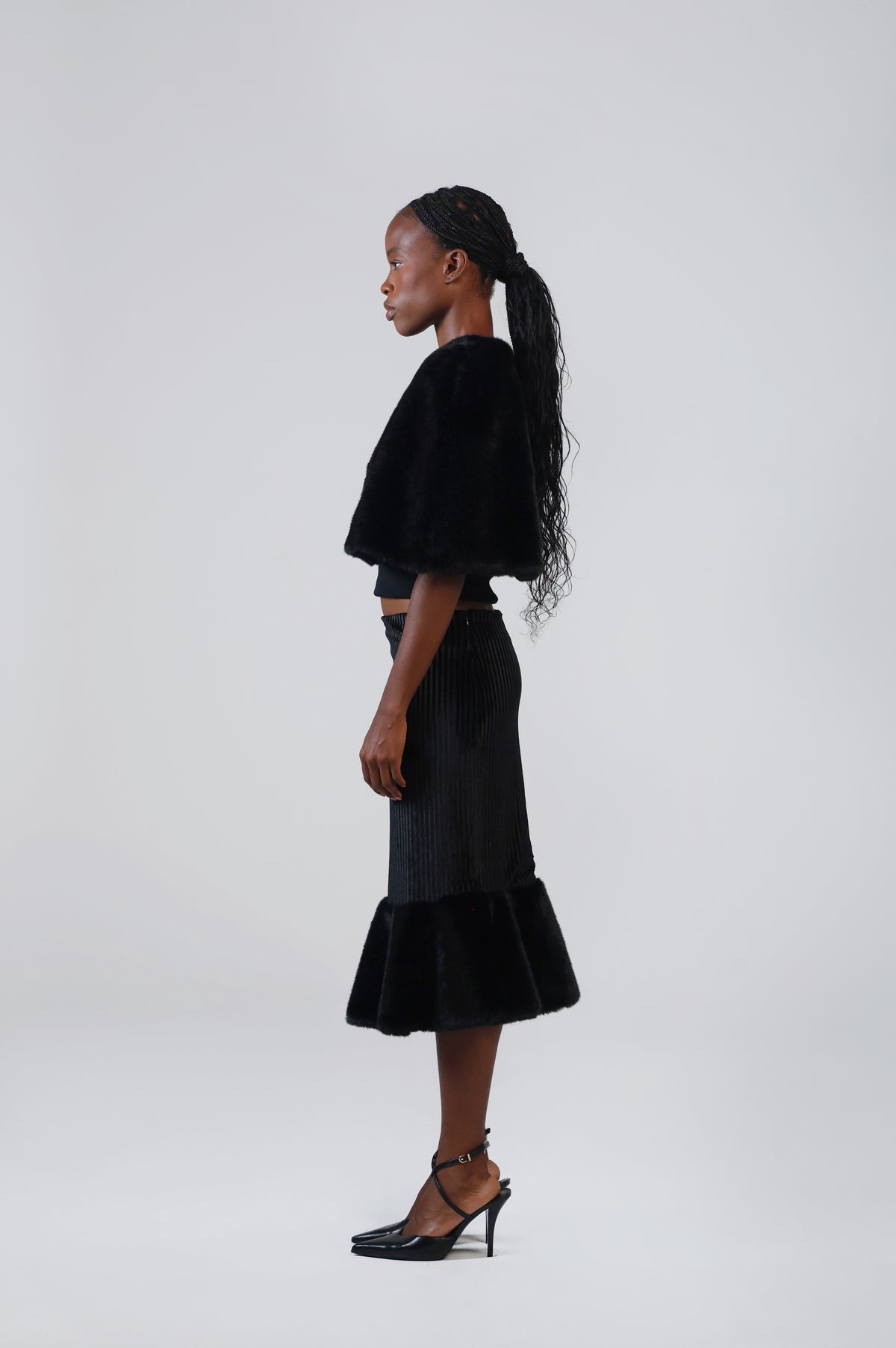 Black velvet midi skirt with faux fur flounce, side view on model, showing the fitted hip and flared hem