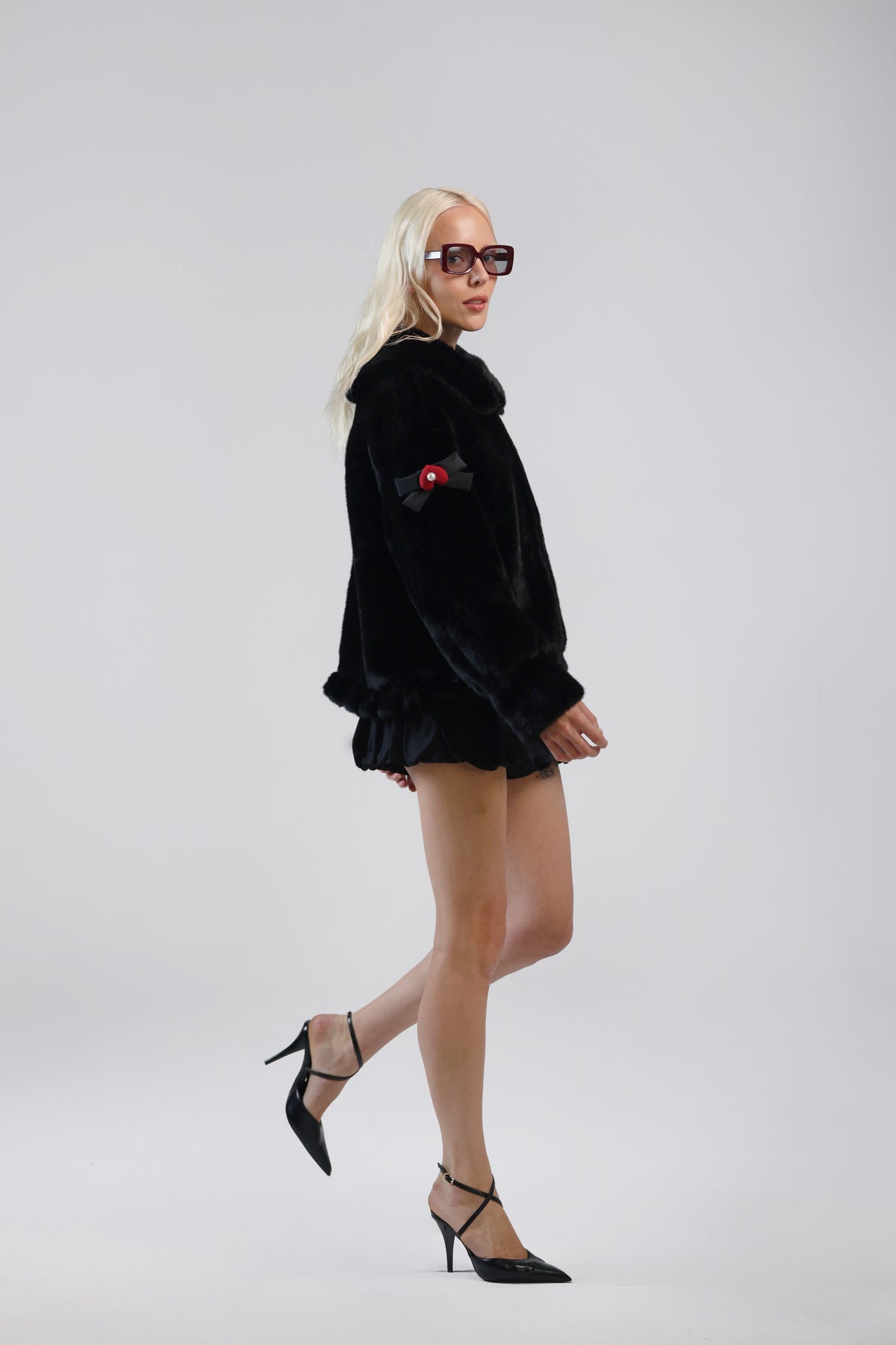 Model in the Jinnette black faux fur jacket with a lacquer black bow charm on the sleeve, side view