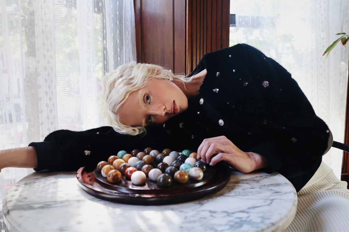 Model resting her head beside a board of stone marbles in the Pearle faux fur cardigan jacket, Dollhouse AW'26 campaign