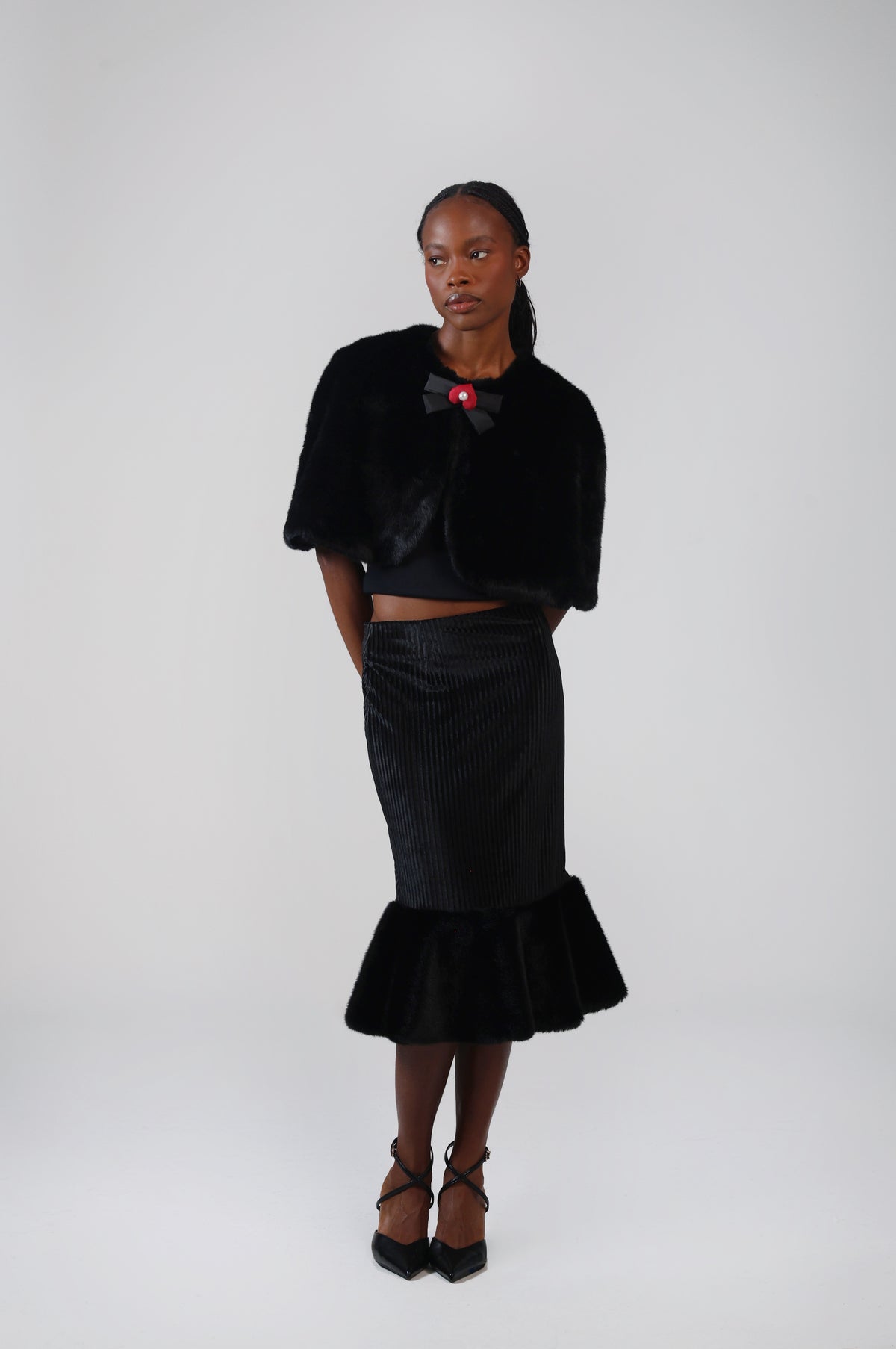 Black faux fur capelet with a lacquer black bow charm at the neckline, worn with a velvet midi skirt with faux fur flounce