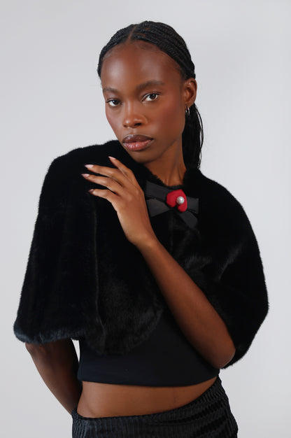 Close-up of the black faux fur capelet on model, with a lacquer black bow charm and red mamu heart logo at the neckline