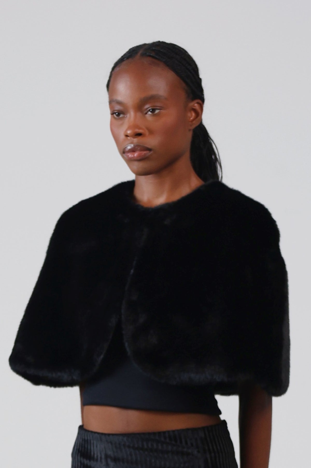 Close-up of the black faux fur capelet's plush pile and curved front edge, three-quarter view