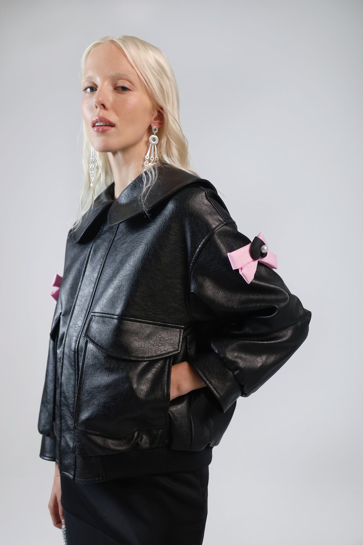 Model in the Jinnoir black faux leather jacket with a pink bow charm on the sleeve, three-quarter view