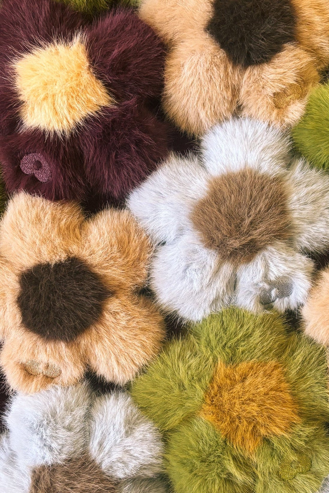 Close-up of a pile of Blume faux fur flower charms in blue, green, brown and mustard tones