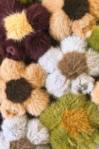Close-up of a pile of Blume faux fur flower charms in blue, green, brown and mustard tones