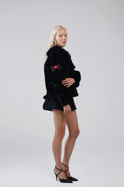 Jinnette black faux fur jacket with lacquer black bow charms on both sleeves, side view on model